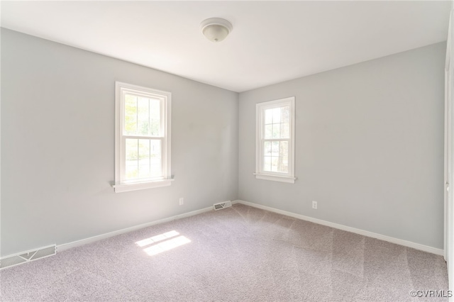 carpeted empty room featuring baseboards, visible vents, and a healthy amount of sunlight