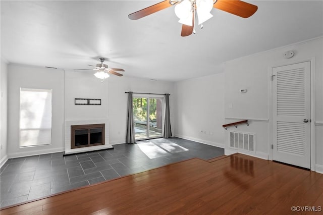 unfurnished living room with ceiling fan, a glass covered fireplace, baseboards, visible vents, and dark wood-style floors