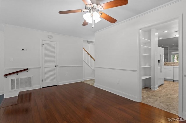 unfurnished living room featuring a ceiling fan, visible vents, crown molding, wood finished floors, and stairs