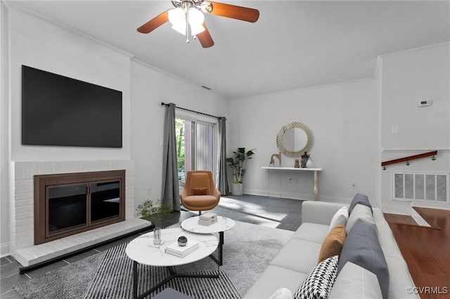 living area featuring crown molding, ceiling fan, a brick fireplace, baseboards, and visible vents