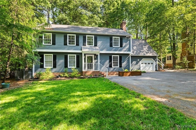 colonial-style house with a garage, a chimney, asphalt driveway, and a front yard