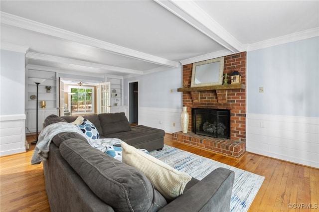living area featuring hardwood / wood-style floors, beam ceiling, wainscoting, crown molding, and a fireplace
