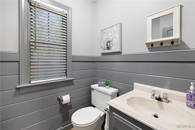 half bath featuring toilet, vanity, and wainscoting