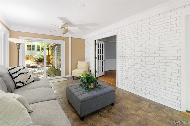 living area with ceiling fan, brick wall, and ornamental molding