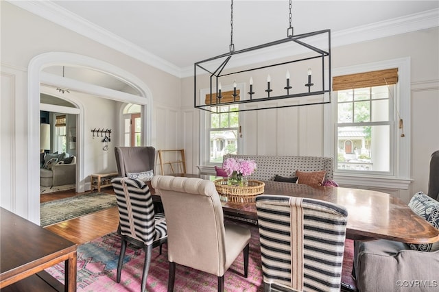 dining space featuring ornamental molding, healthy amount of natural light, wood finished floors, and arched walkways