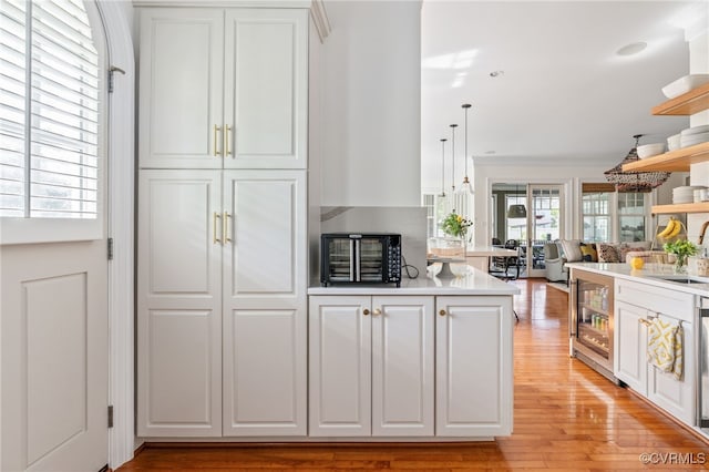 kitchen featuring white cabinetry, beverage cooler, a sink, light wood-style flooring, and ornamental molding