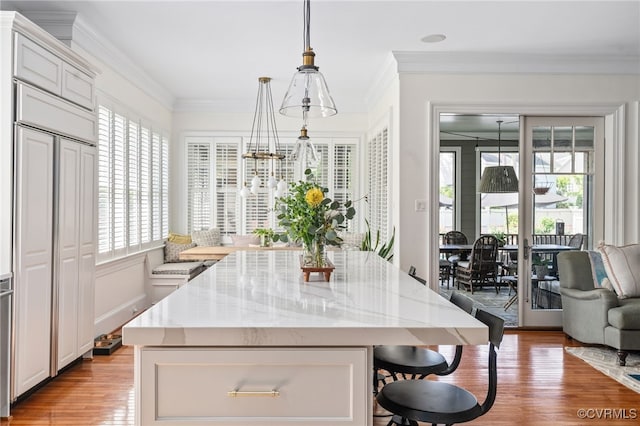kitchen featuring a kitchen breakfast bar, light wood-style floors, a kitchen island, light stone countertops, and hanging light fixtures
