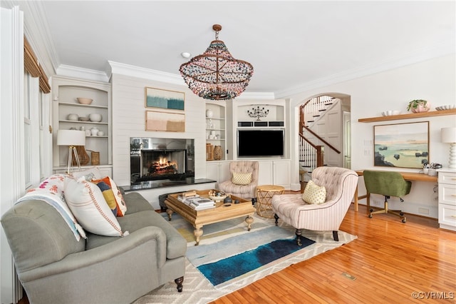 living area with ornamental molding, stairs, a warm lit fireplace, hardwood / wood-style floors, and arched walkways
