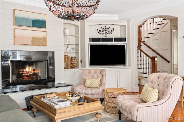 living room featuring stairs, ornamental molding, a chandelier, wood finished floors, and built in shelves