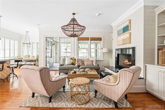 living area with a chandelier, light wood-style floors, crown molding, and a glass covered fireplace