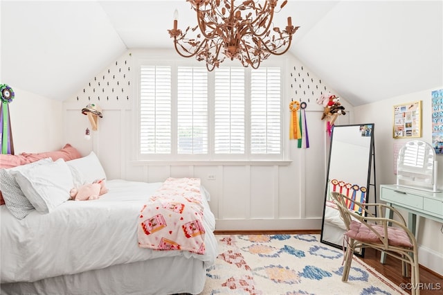 bedroom featuring lofted ceiling, a chandelier, wood finished floors, and a decorative wall