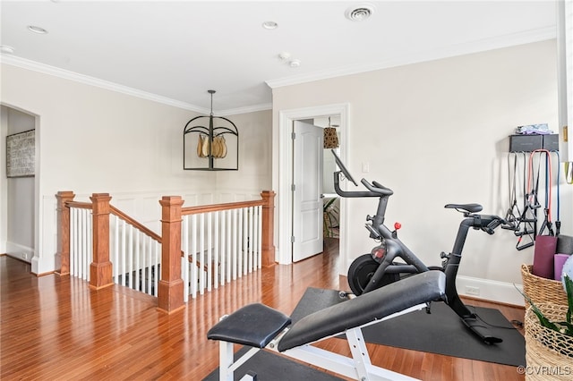 exercise area with ornamental molding, wood finished floors, arched walkways, a chandelier, and baseboards