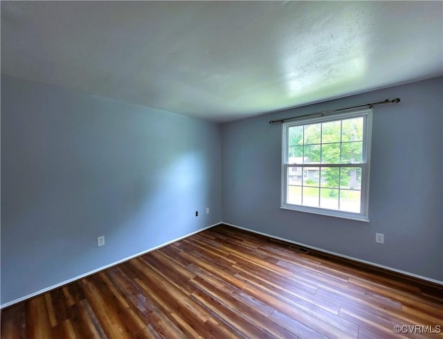 spare room featuring dark wood-style flooring and baseboards