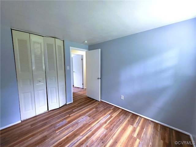 unfurnished bedroom with wood finished floors, a closet, and baseboards