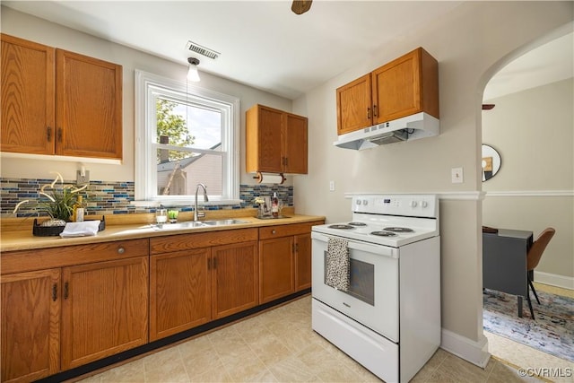 kitchen featuring electric stove, under cabinet range hood, a sink, brown cabinetry, and tasteful backsplash