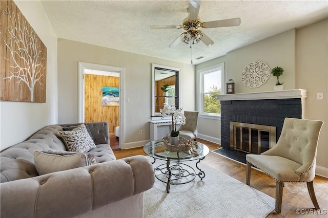 living area with a ceiling fan, a fireplace, wood finished floors, baseboards, and a textured ceiling
