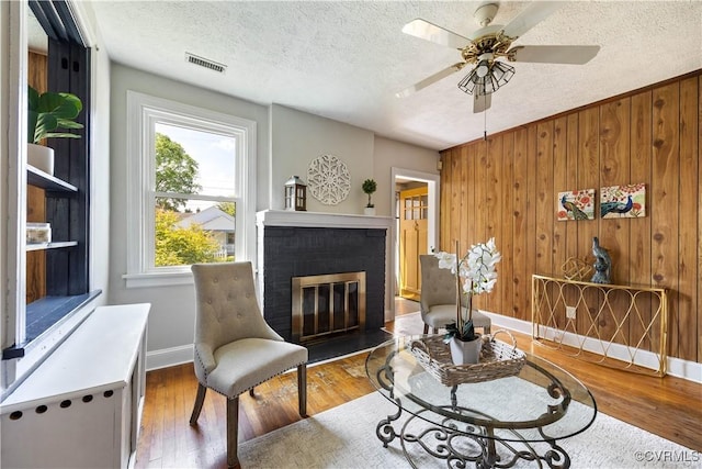 sitting room with a textured ceiling, ceiling fan, a brick fireplace, wood finished floors, and baseboards