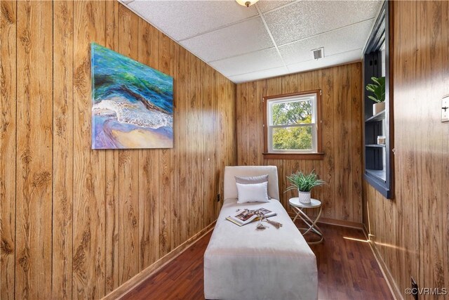 living area with wood walls, a drop ceiling, baseboards, and wood finished floors