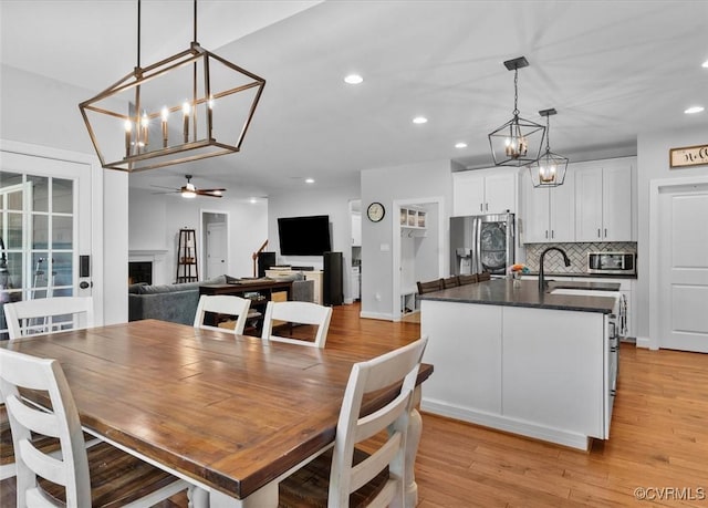 dining room featuring recessed lighting, light wood finished floors, ceiling fan with notable chandelier, and a fireplace