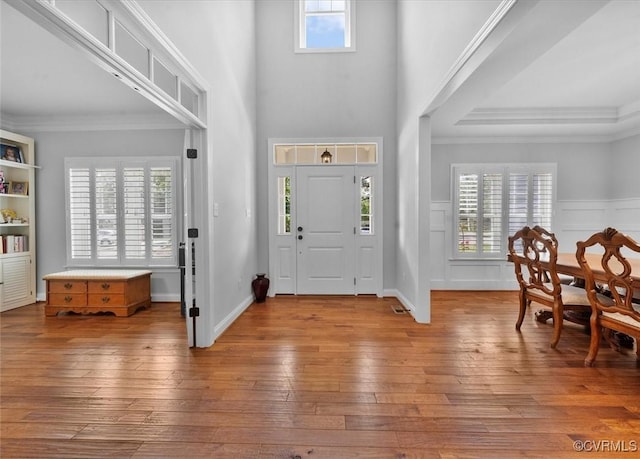 entryway featuring a towering ceiling, visible vents, a wainscoted wall, ornamental molding, and hardwood / wood-style floors