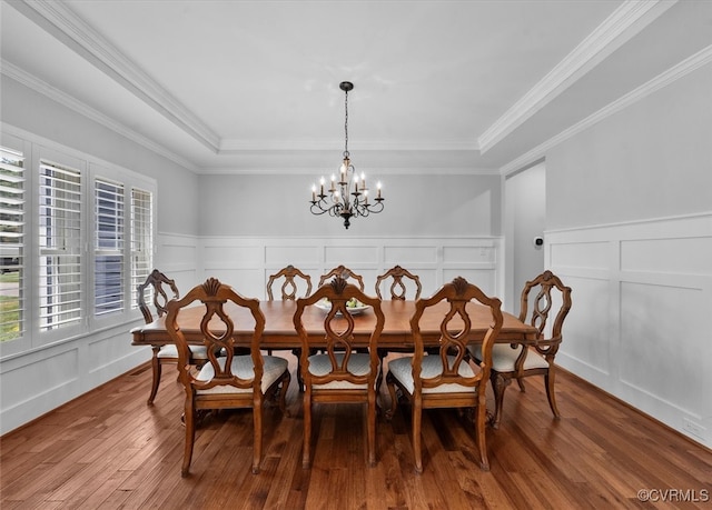 dining space with crown molding, wood finished floors, a decorative wall, a wainscoted wall, and a notable chandelier