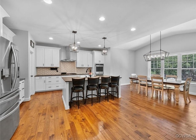 kitchen featuring decorative backsplash, a kitchen bar, a notable chandelier, stainless steel appliances, and wall chimney exhaust hood
