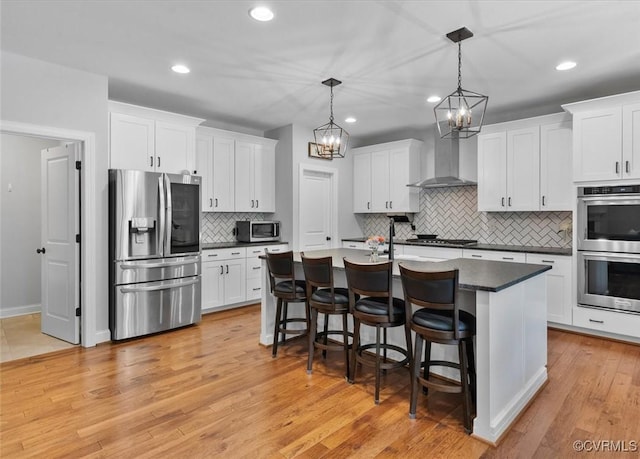 kitchen with dark countertops, wall chimney range hood, white cabinets, tasteful backsplash, and appliances with stainless steel finishes