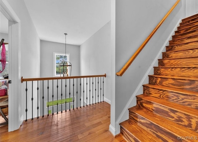 stairs featuring an inviting chandelier, baseboards, and wood finished floors
