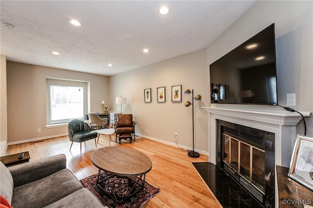 living room with wood finished floors, recessed lighting, a fireplace with flush hearth, and baseboards