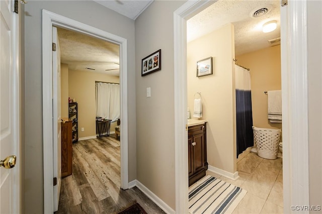 corridor featuring a textured ceiling, baseboards, and light wood-style flooring