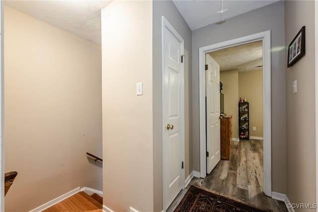 hall with an upstairs landing, wood finished floors, baseboards, and a textured ceiling