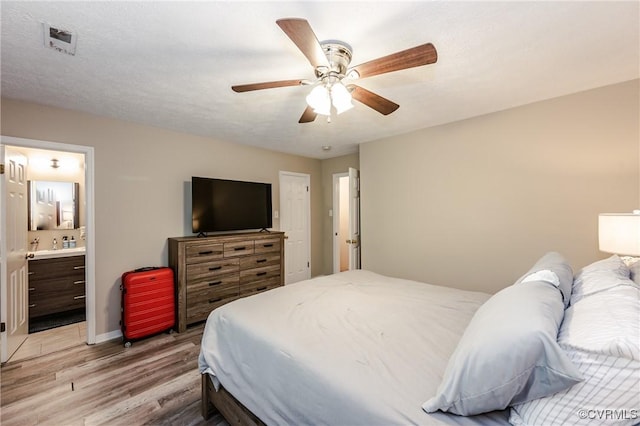 bedroom featuring light wood finished floors, ceiling fan, baseboards, and ensuite bathroom