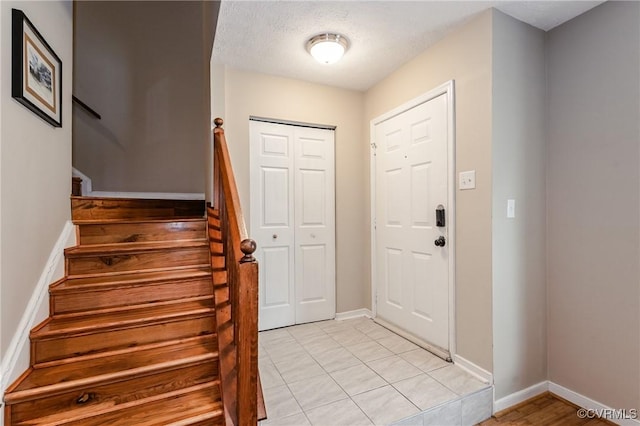 foyer featuring stairway, baseboards, light tile patterned flooring, and a textured ceiling