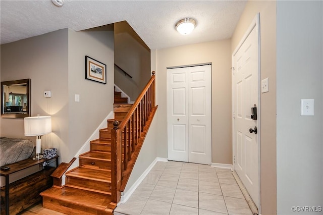 foyer featuring stairs, baseboards, a textured ceiling, and light tile patterned floors