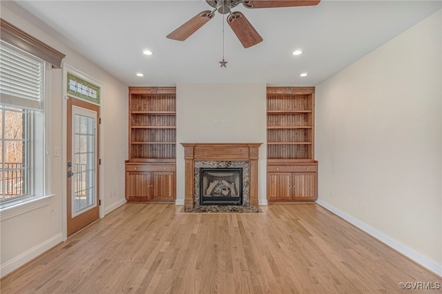 unfurnished living room with light wood-style floors, baseboards, a ceiling fan, and a high end fireplace
