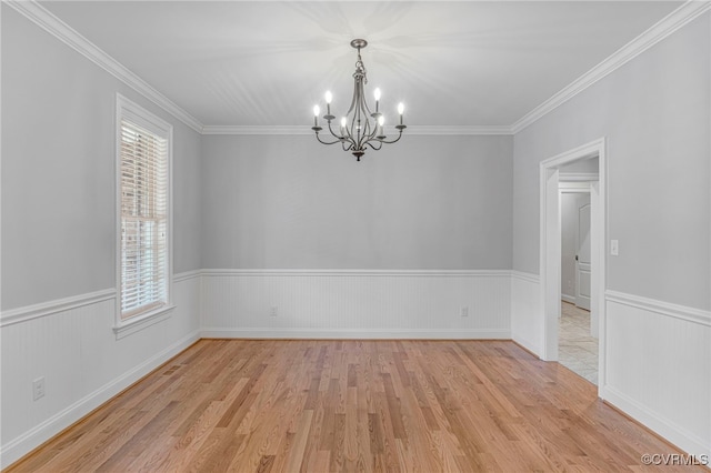 spare room featuring a notable chandelier, wainscoting, crown molding, and light wood-style floors