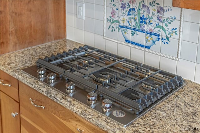 interior details featuring stainless steel gas cooktop, light stone countertops, decorative backsplash, and brown cabinetry