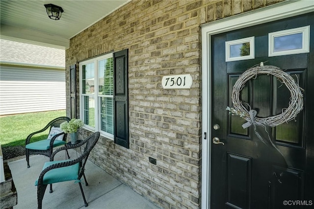 view of exterior entry featuring a porch and brick siding