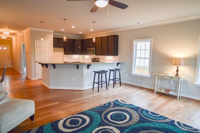 kitchen with crown molding, stainless steel microwave, a kitchen bar, and light wood finished floors