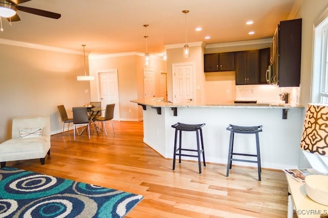 kitchen featuring crown molding, light stone countertops, decorative light fixtures, and light wood finished floors