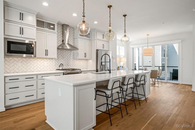 kitchen featuring decorative backsplash, black microwave, stove, wall chimney exhaust hood, and an island with sink