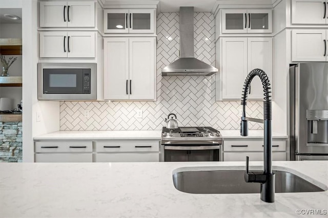 kitchen featuring backsplash, stainless steel appliances, wall chimney exhaust hood, and light stone countertops