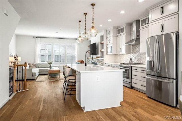 kitchen with a kitchen island with sink, light countertops, wall chimney exhaust hood, a sink, and stainless steel appliances
