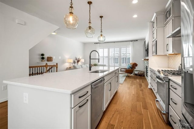 kitchen with appliances with stainless steel finishes, a sink, light countertops, an island with sink, and light wood-style flooring