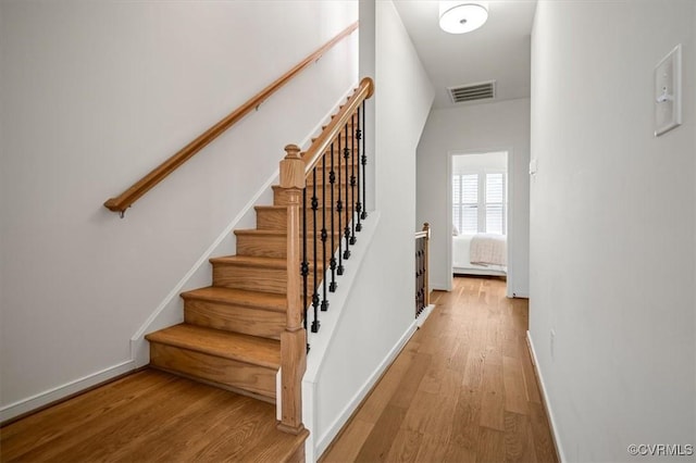 stairway with baseboards, wood finished floors, and visible vents