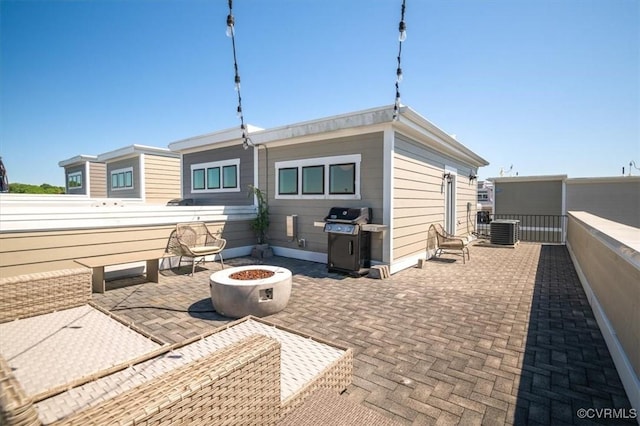 rear view of property with central AC unit, a patio area, fence, and a fire pit