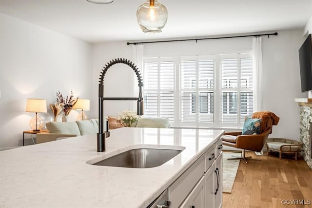 kitchen with a sink, white cabinets, light wood finished floors, and a wealth of natural light
