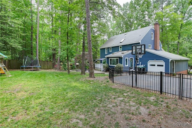 view of yard with a trampoline, driveway, a garage, a fenced backyard, and a playground