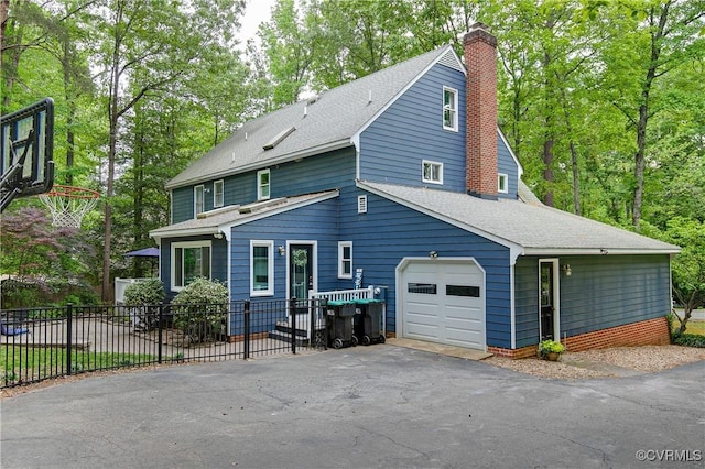view of front of house featuring a chimney, fence, an attached garage, a shingled roof, and aphalt driveway
