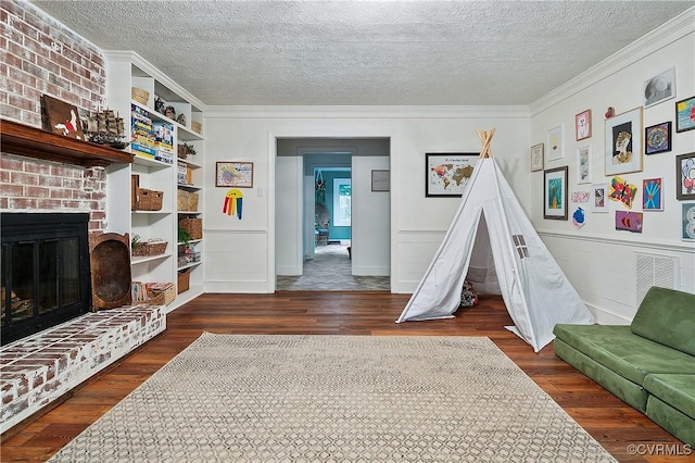 living area featuring ornamental molding, a fireplace, a textured ceiling, and wood finished floors